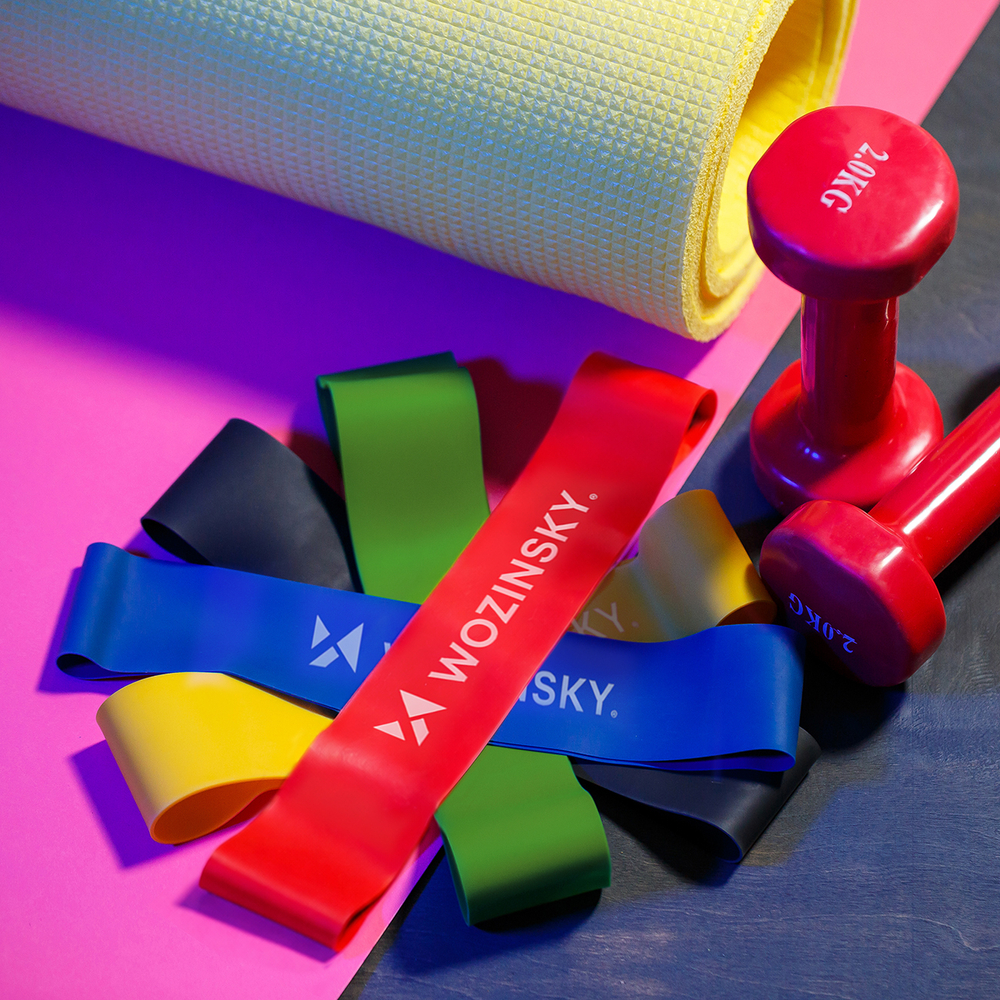 Red dumbbells, fitness mat and elastic bands for sports on a pink background. Healthy lifestyle.