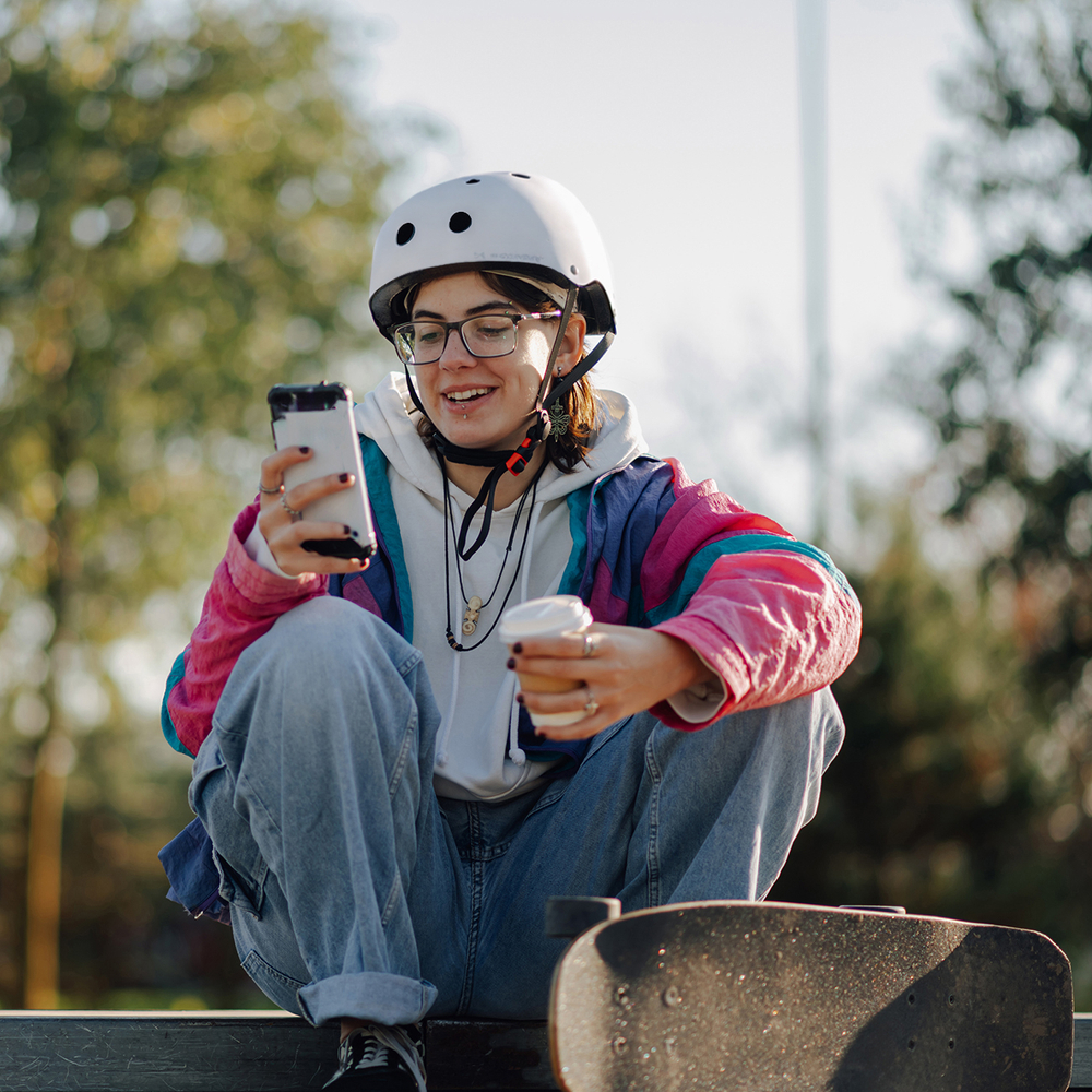 Smiling skater using smartphone and drinking coffee in skatepark