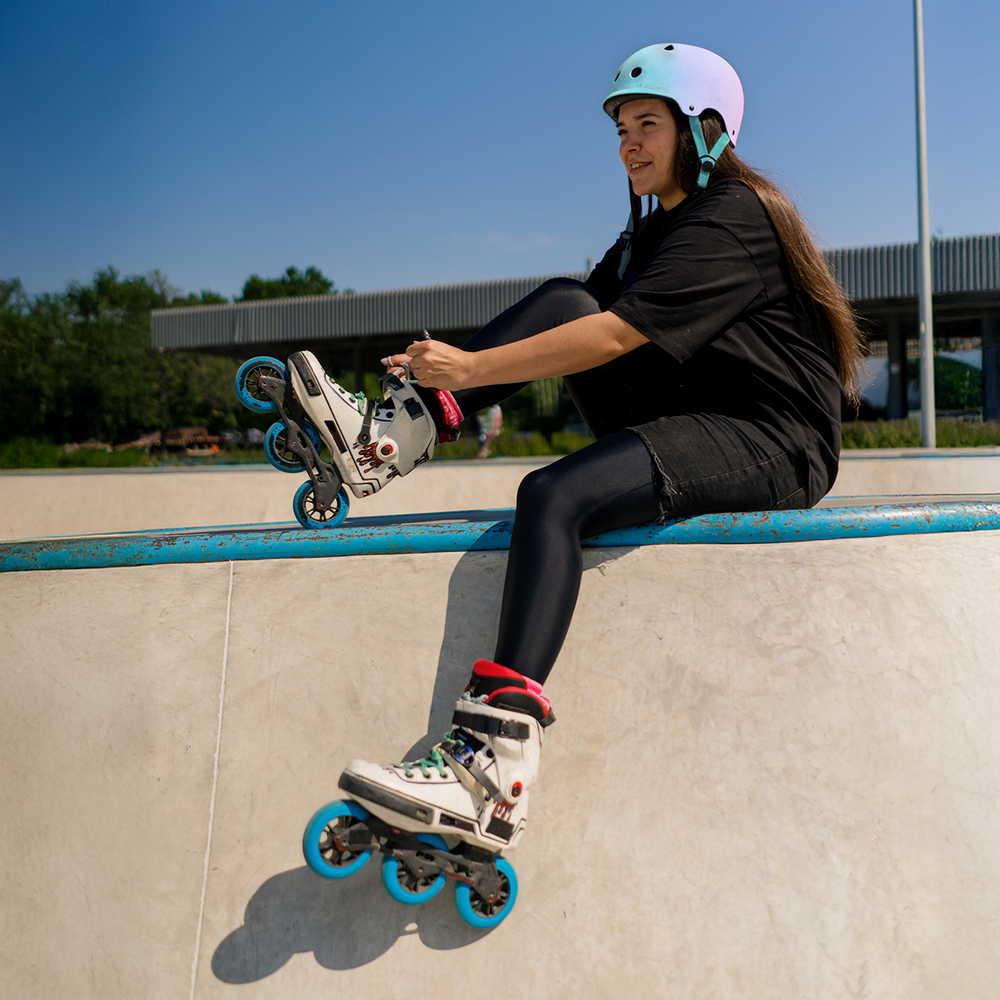 young hipster girl in protective helmet on roller skates tying l
