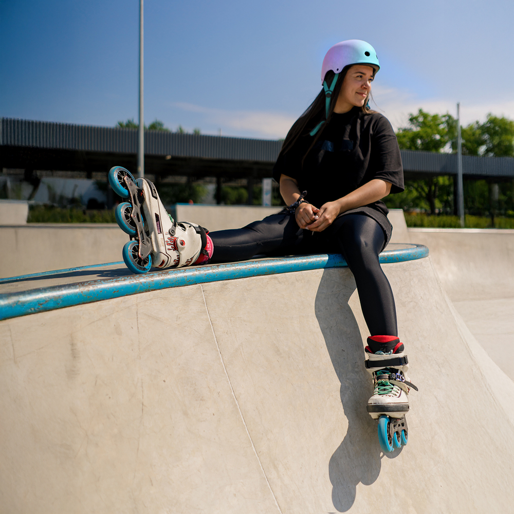 young hipster girl in protective helmet on roller skates sitting
